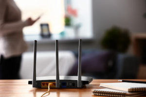 A router sits on a desk with notebooks and a pencil