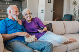 Older couple sitting on couch eating popcorn watching live TV streaming service